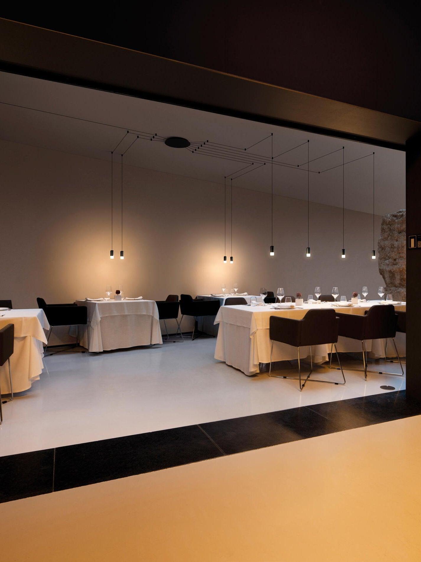 Lit pendant heads and black cable lines above restaurant booths and dining tables