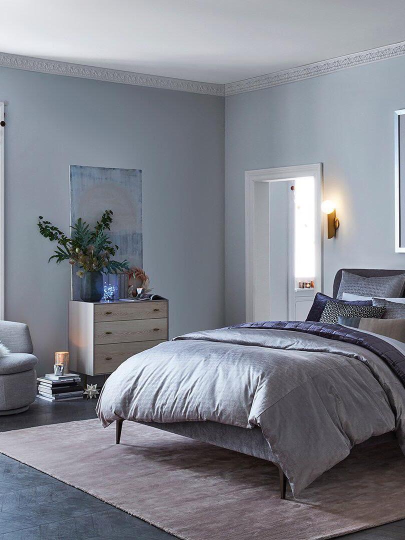 Bedroom view with lit globe wall lamp beside a doorway near an upholstered bed, dresser and armchair