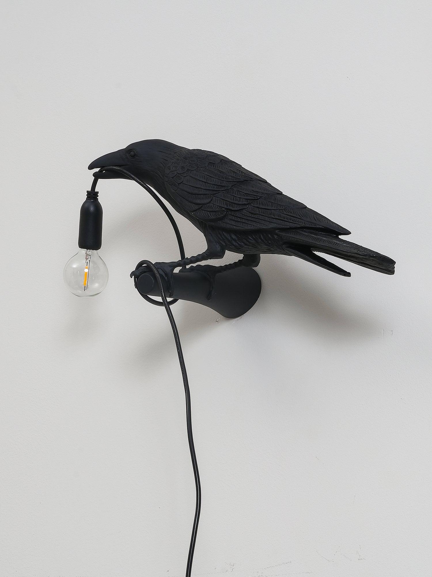Black bird wall light with an unlit clear filament-style bulb and looped trailing cord