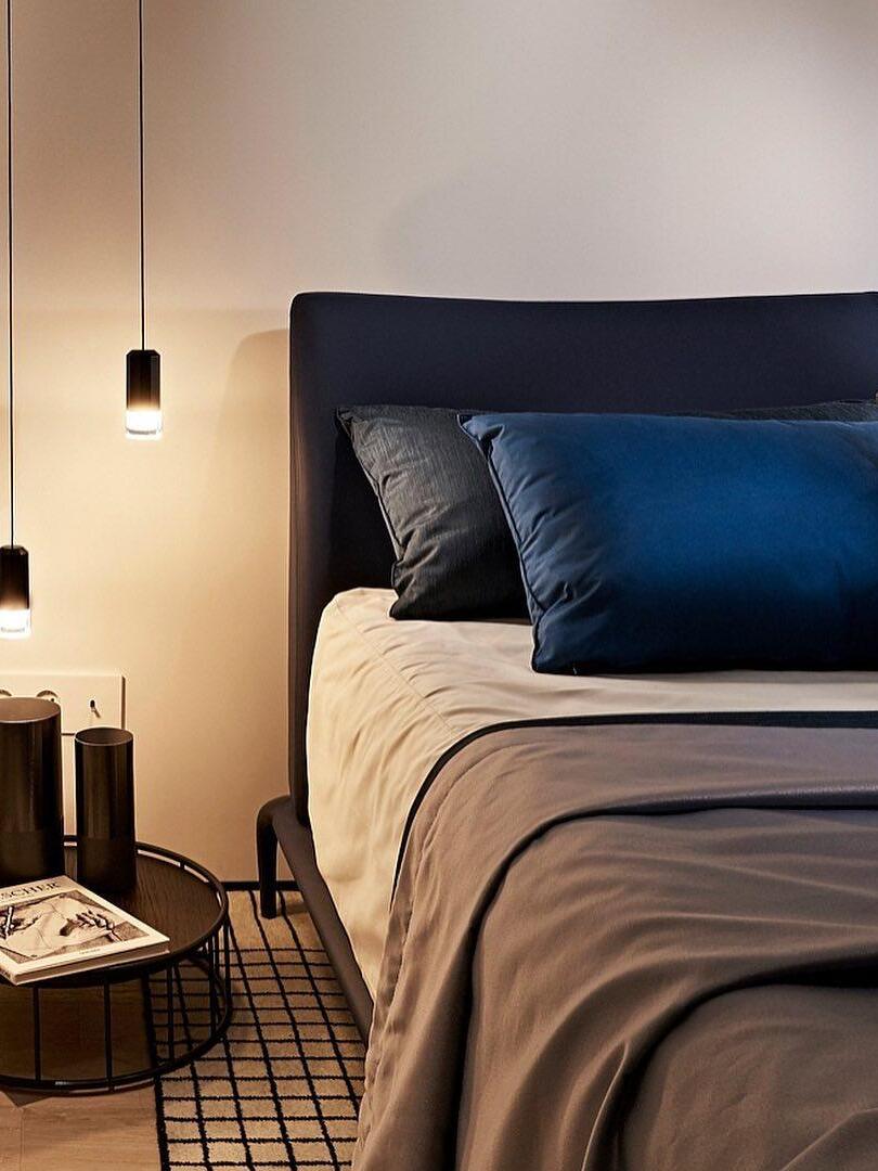 Single lit black pendant beside a blue upholstered bed and small side table