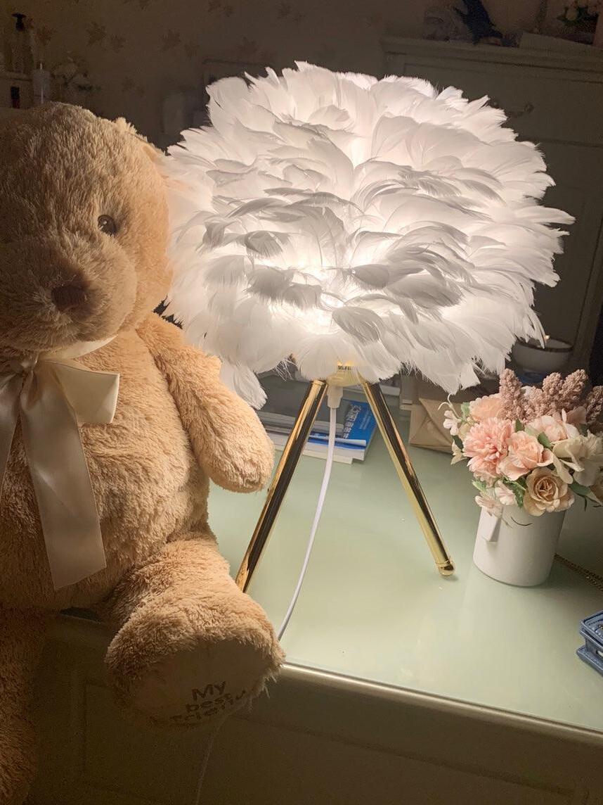White feather lamp beside teddy bear and flowers