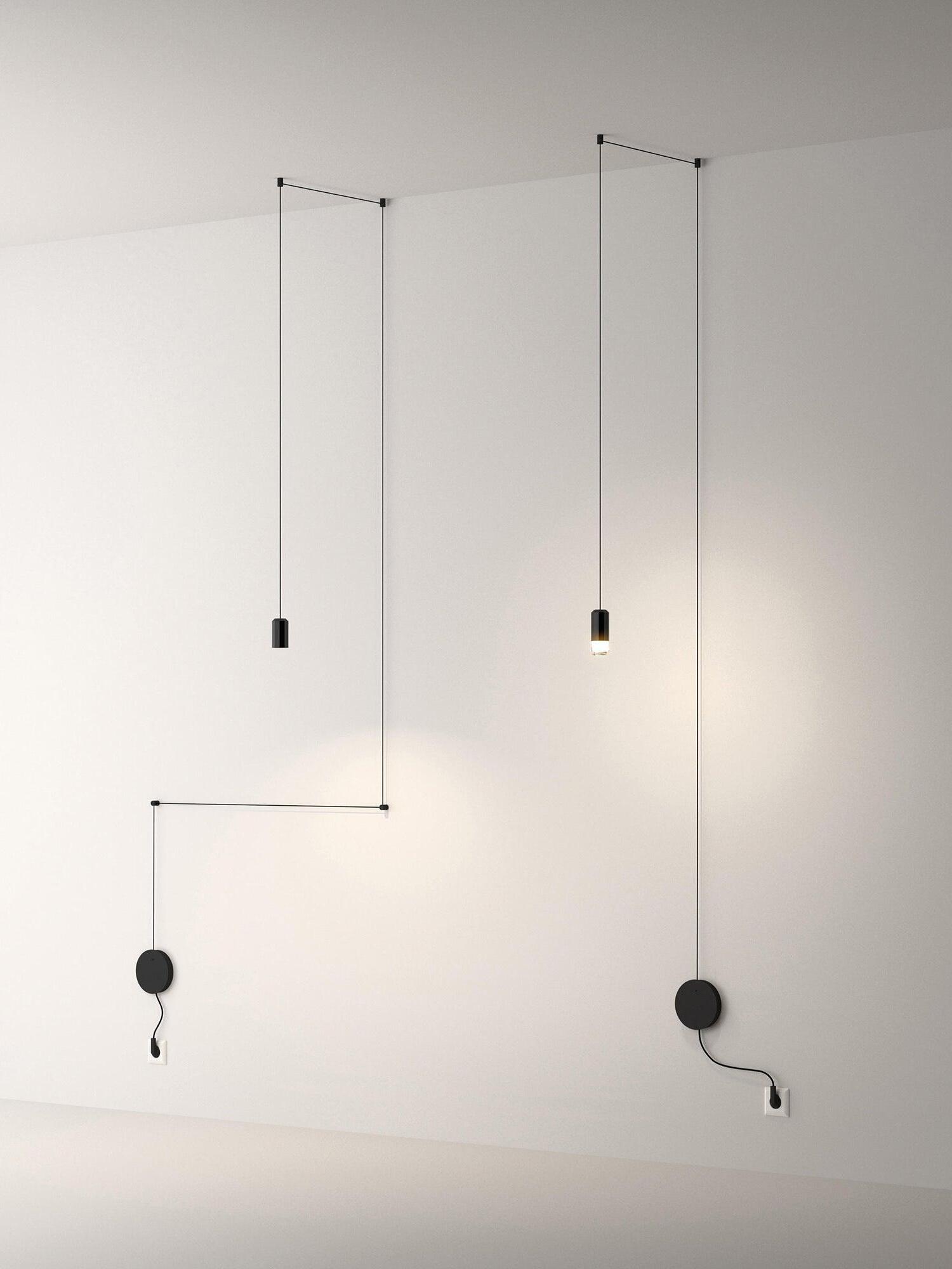 Two lit single-head cable pendants with wall plates on a pale wall