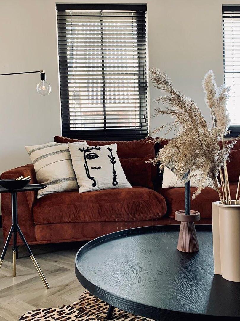 Cropped black wall-lamp arm and clear bulb above a rust sofa with patterned cushions