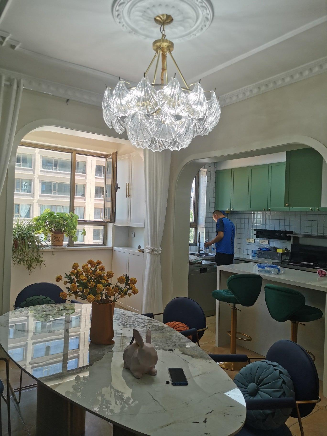 Glass light over a dining table with blue chairs and flowers against a green wall