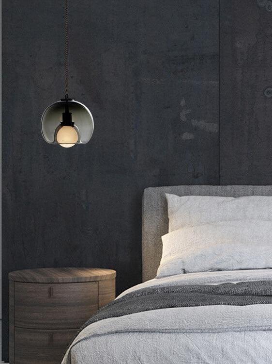 Smoke-toned Eres pendant hanging beside a bed against a dark wall.