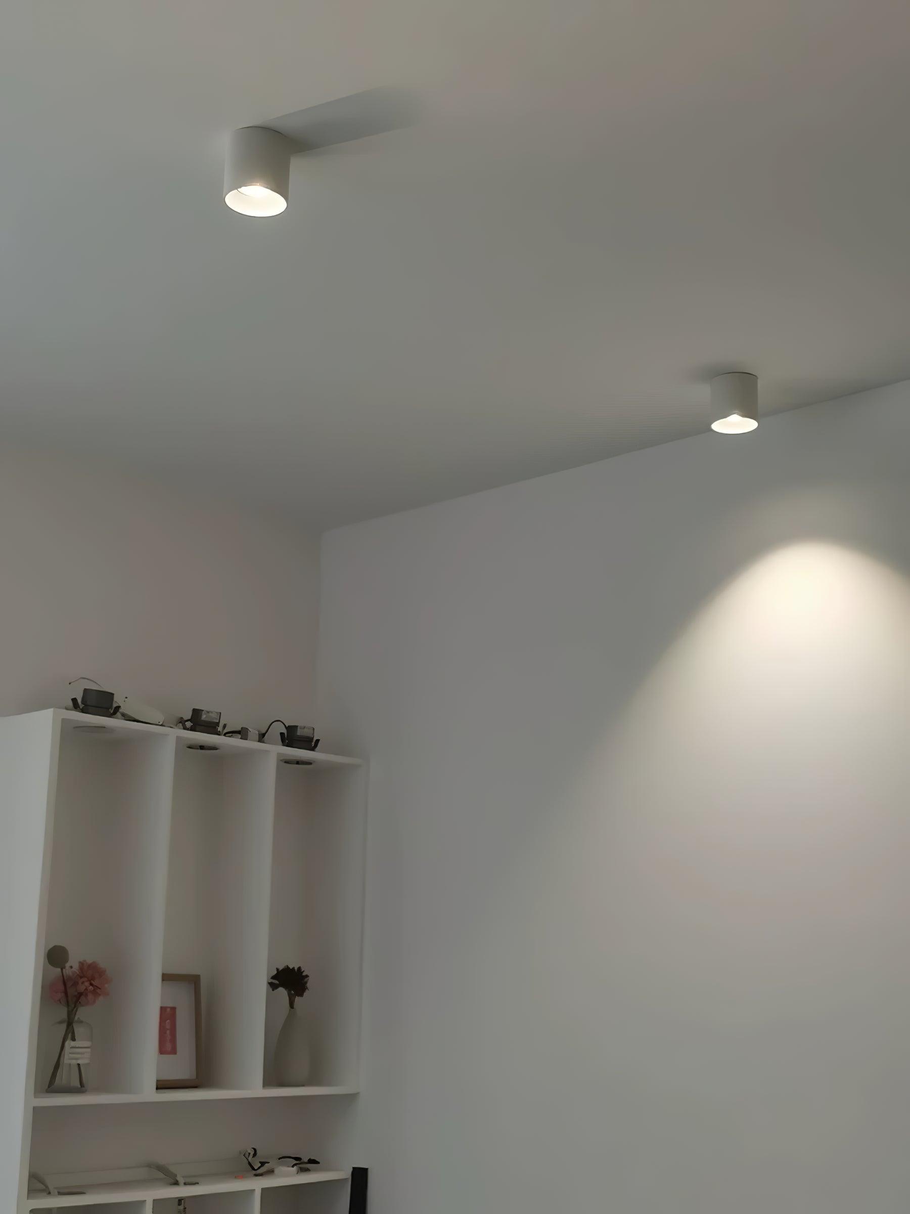 Two white ceiling lights above a storage unit with vases and small dark objects on top, with a light pool on the wall