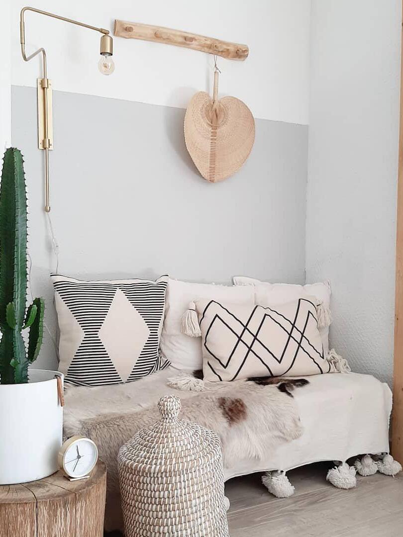 Brass-tone bent-arm wall lamp above a cushioned bench beside a cactus and hanging straw hat