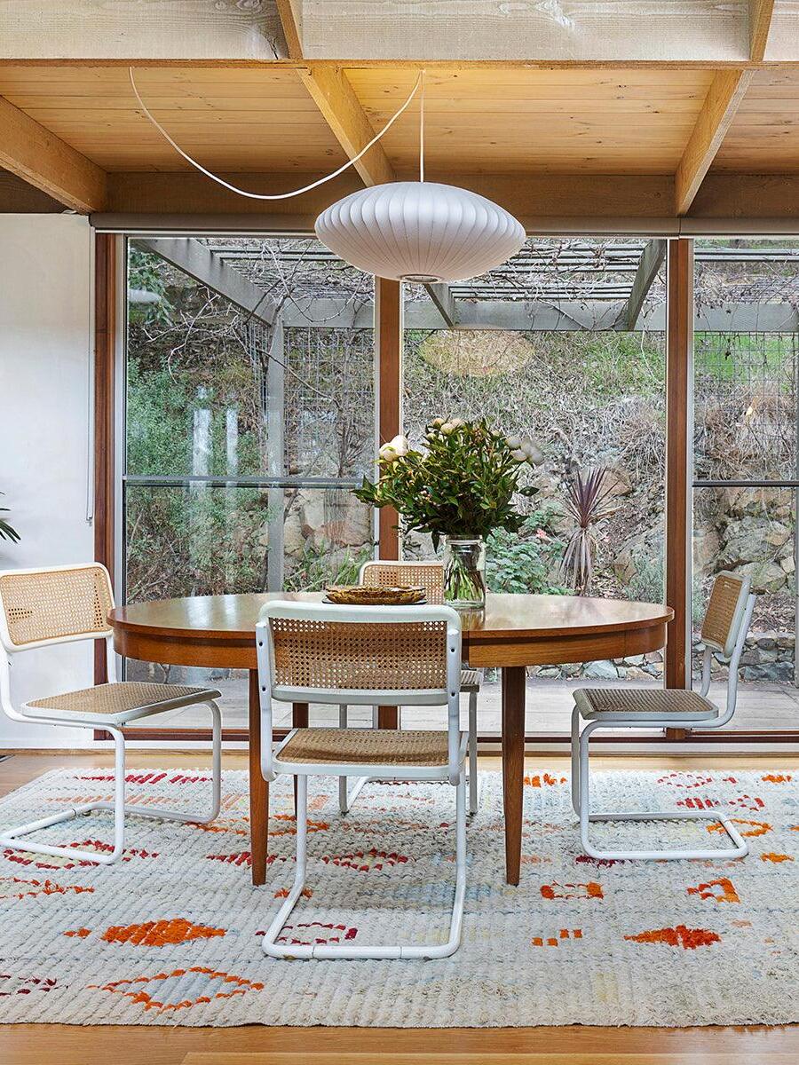 White oval ribbed pendant over a round dining table near large windows with a looped ceiling cord