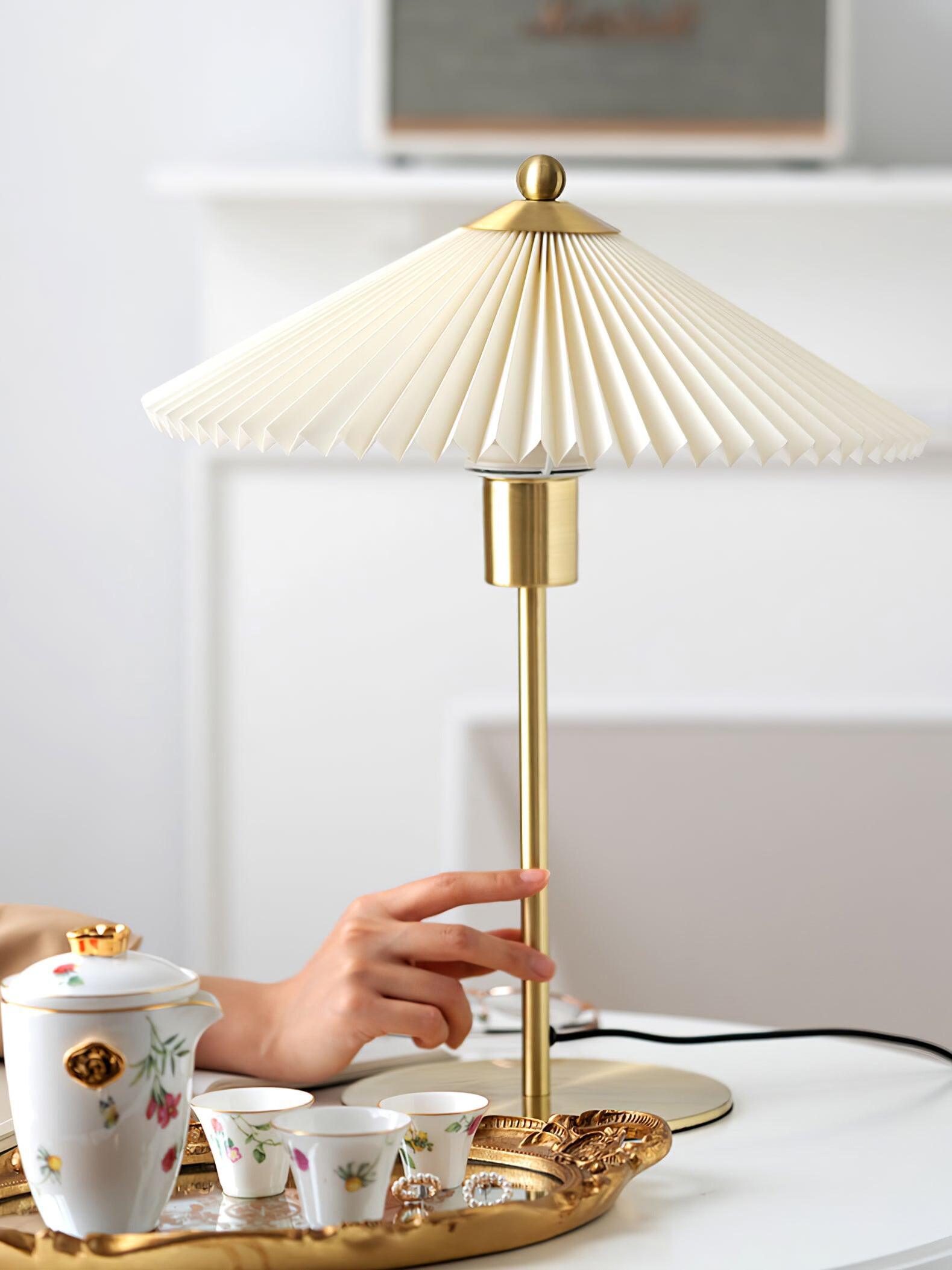 Wider view of a hand near the gold-tone stem and a decorative tea set below the pleated shade