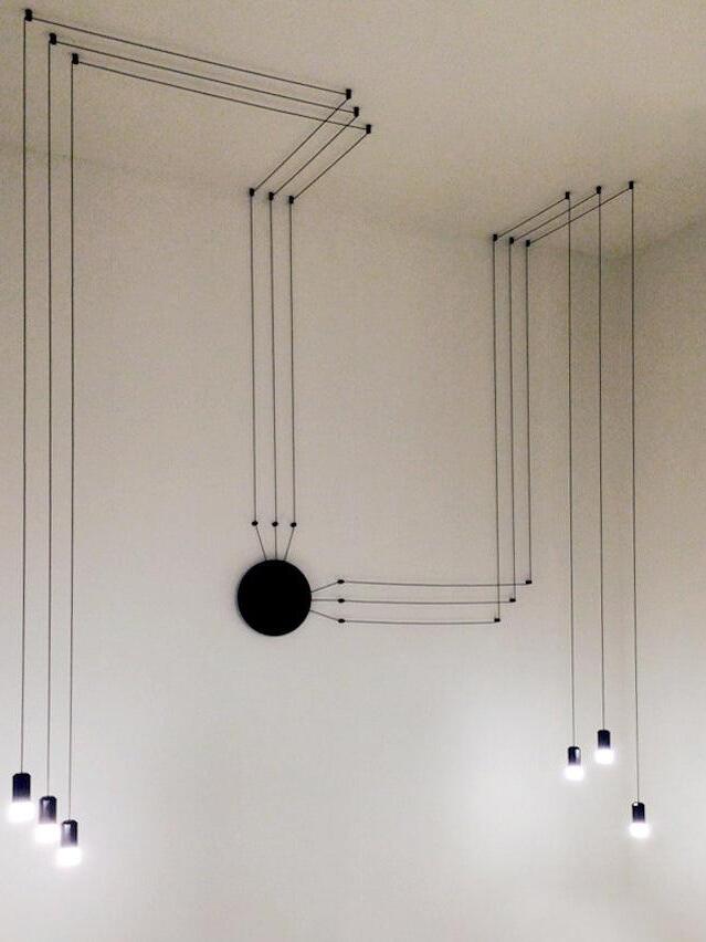 Six black pendant heads with parallel ceiling and wall cables meeting at a round plate