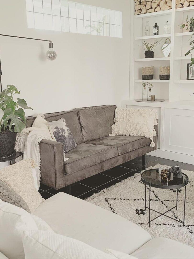Cropped wall-lamp arm and exposed clear bulb above a grey sofa beside white shelving
