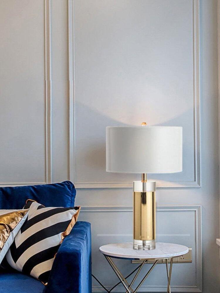 Gold-tone cylindrical lamp on round side table beside blue chair and panelled wall