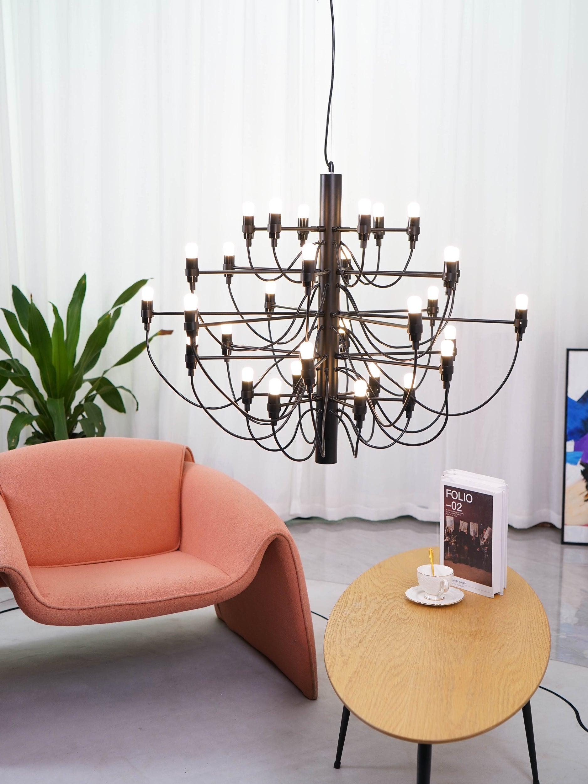 Black chandelier above an oval wooden side table beside a pink chair