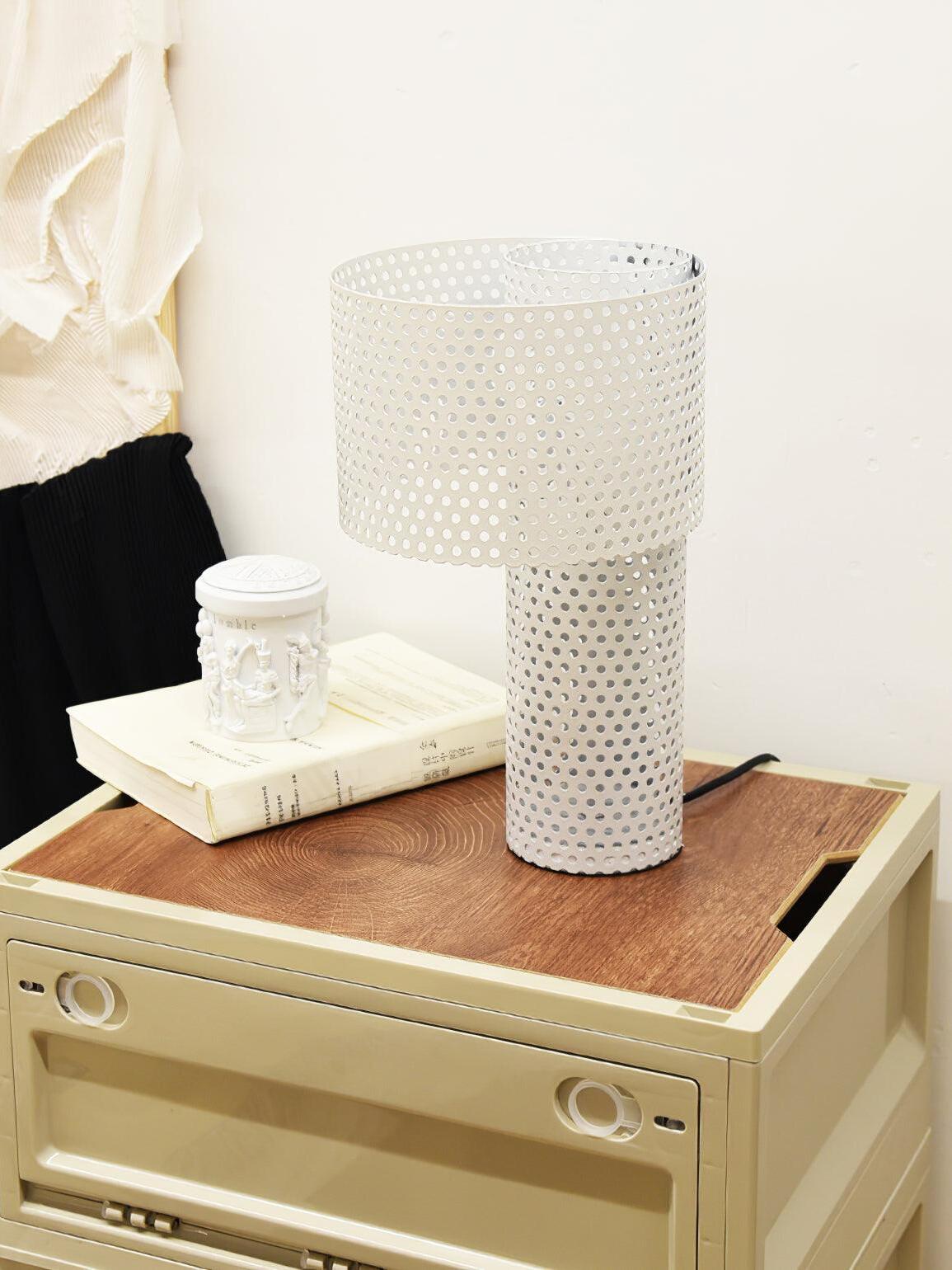 White perforated lamp on wood cabinet beside cup
