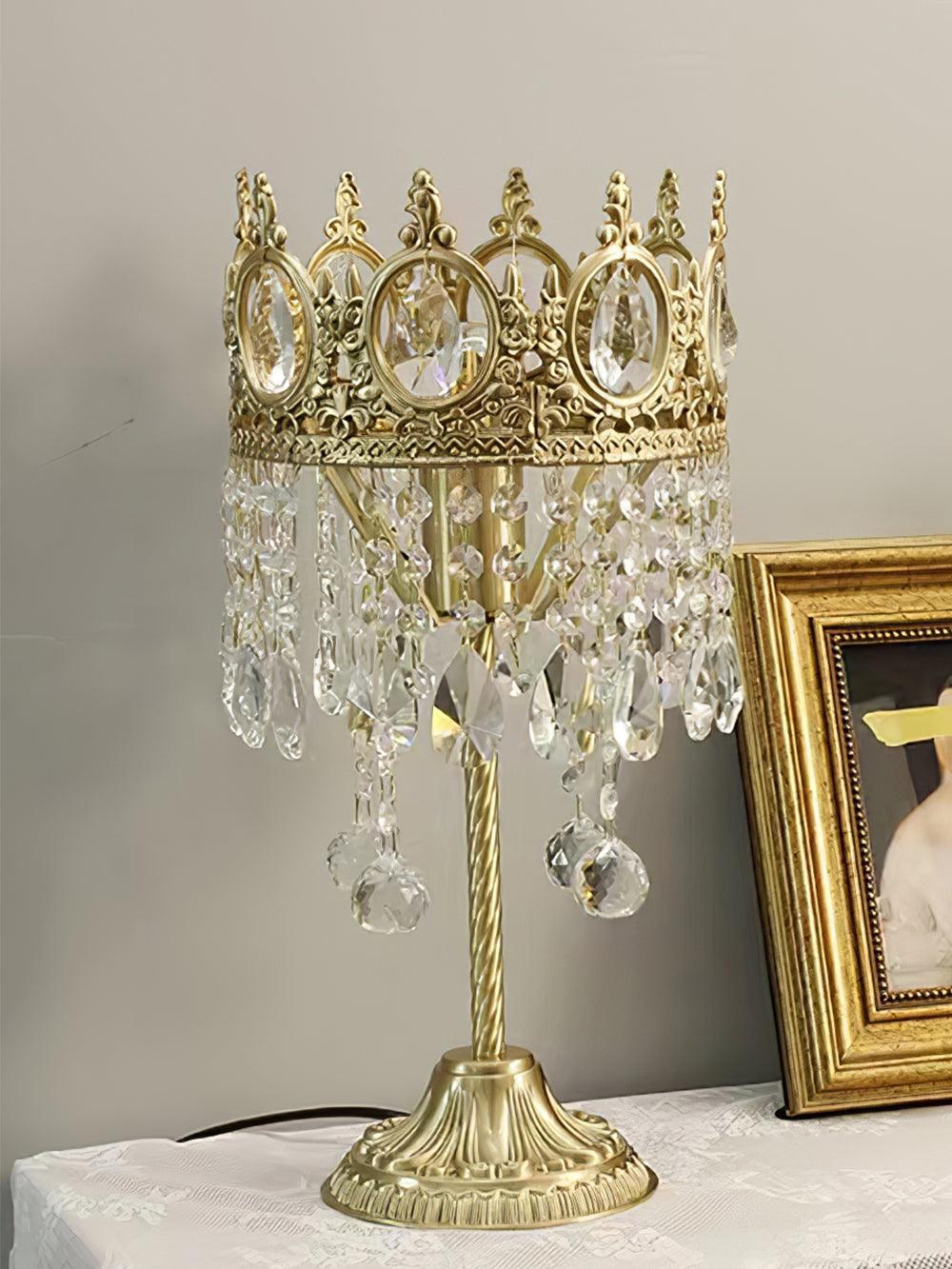 Unlit open-top crown crystal table lamp with layered lower drops beside a framed picture.
