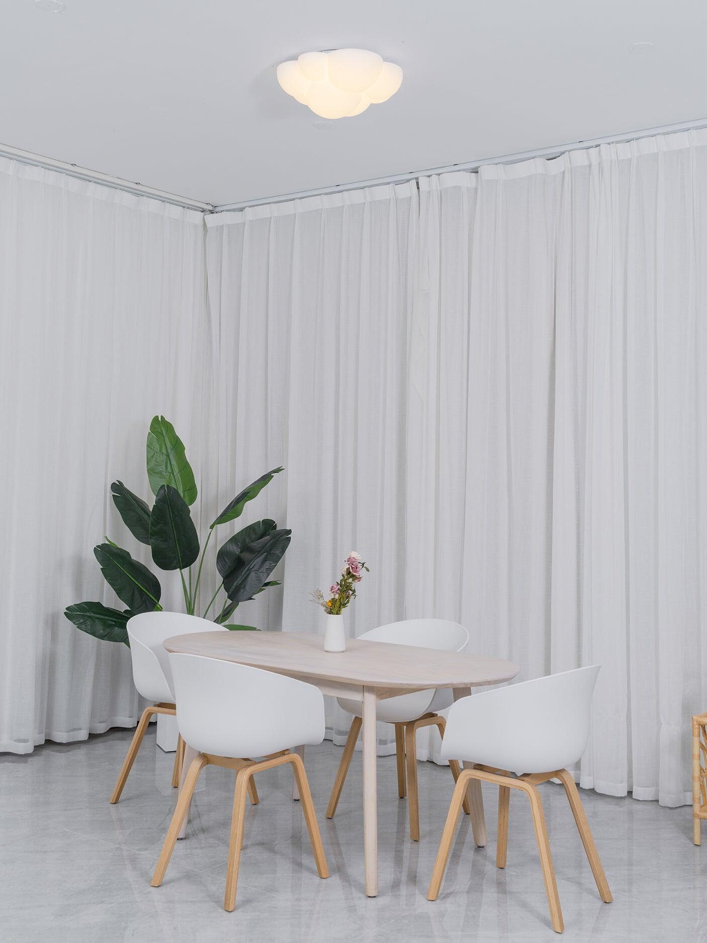 Illuminated Nuage ceiling light above a white dining table with pale chairs and a plant