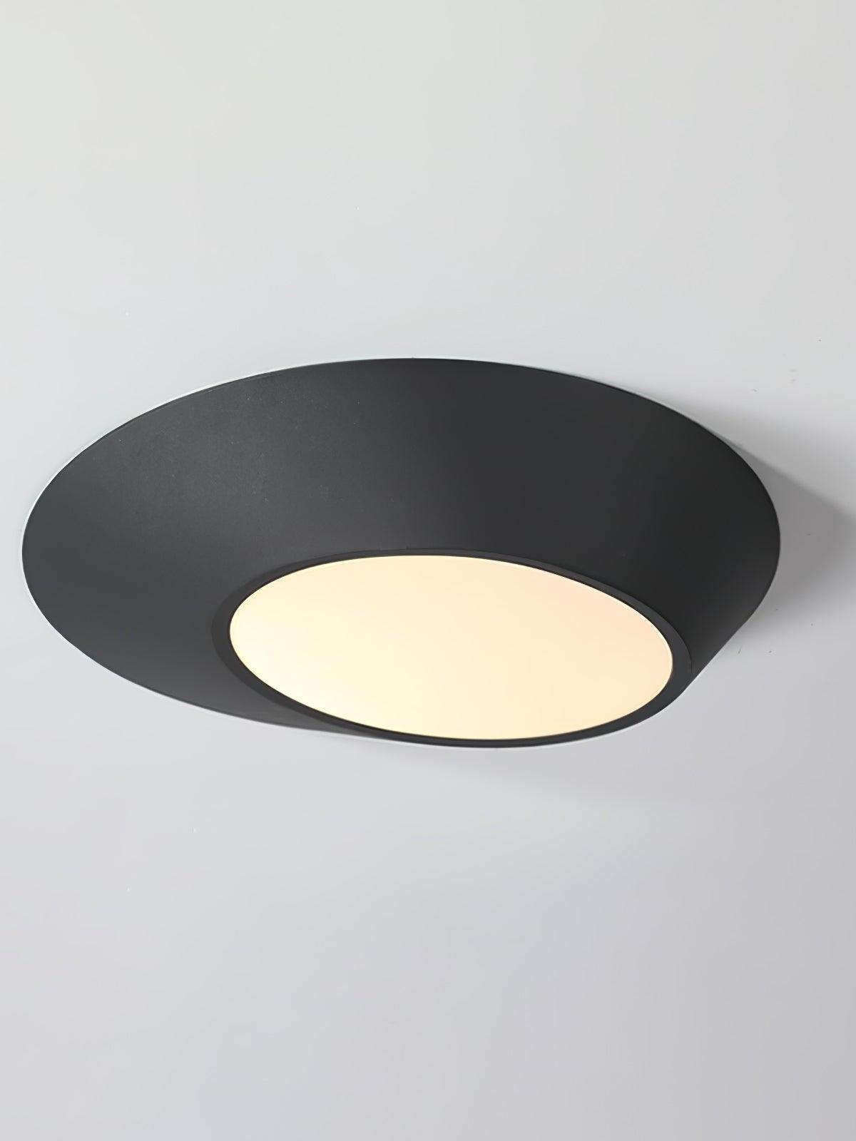 Black angled ceiling light with a warm-looking circular diffuser on a pale background