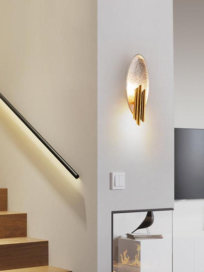 Silver-tone oval wall light with gold tubes beside indoor stairs