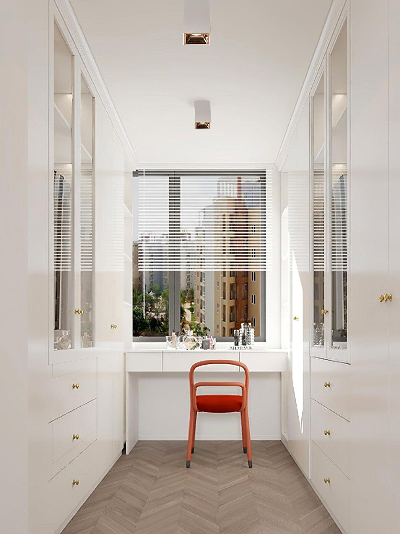 Two white ceiling spots with gold-looking inner cups above an orange chair and white glass-front cabinets