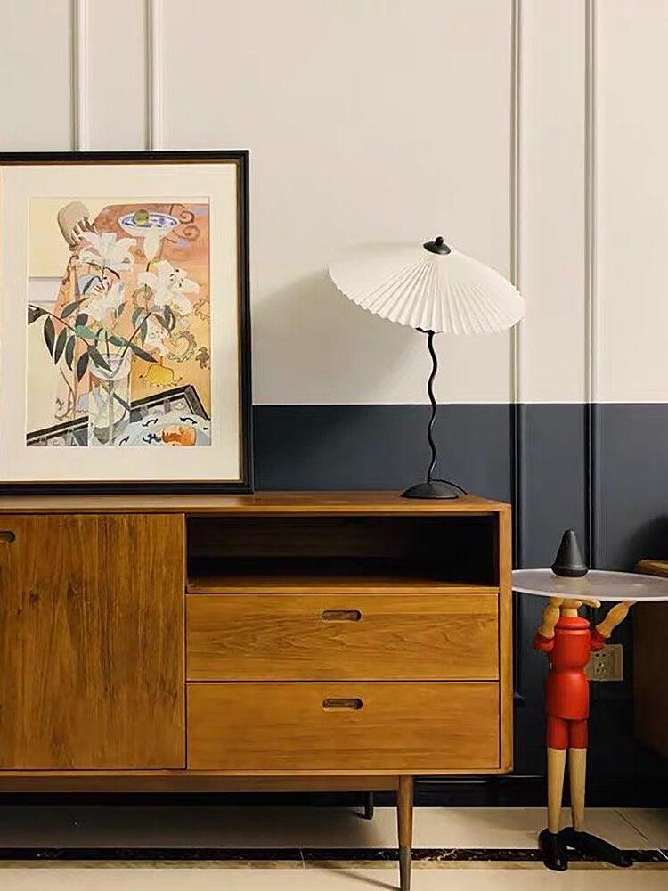 White-shade Squiggle lamp on a wooden sideboard beside framed artwork against a two-tone paneled wall