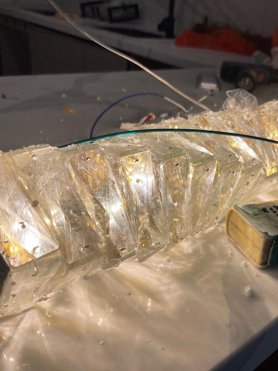 Close view of illuminated crystal pieces with loose wiring and plastic packaging on a work surface