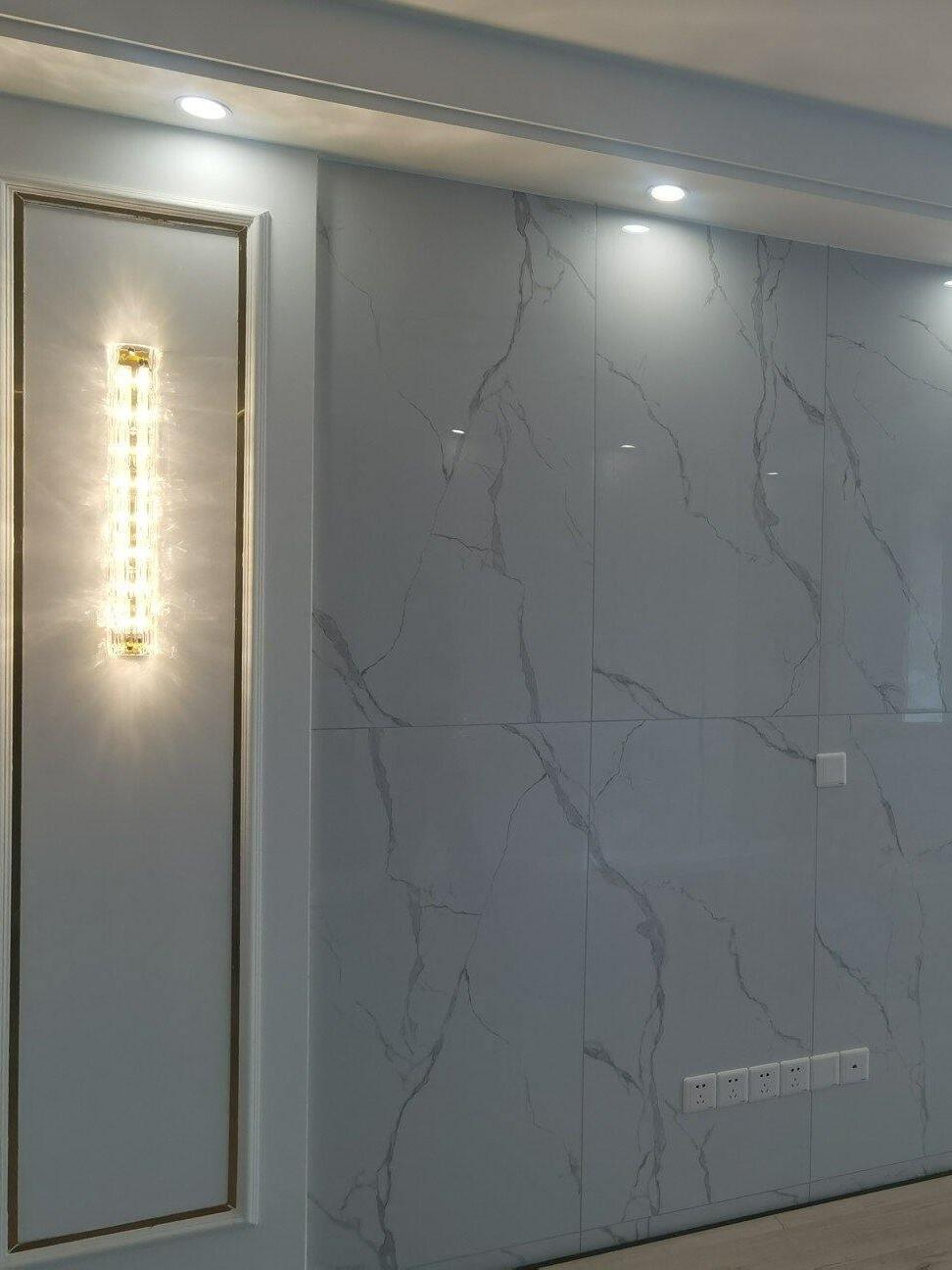 Glass wall light on framed panel beside grey veined wall