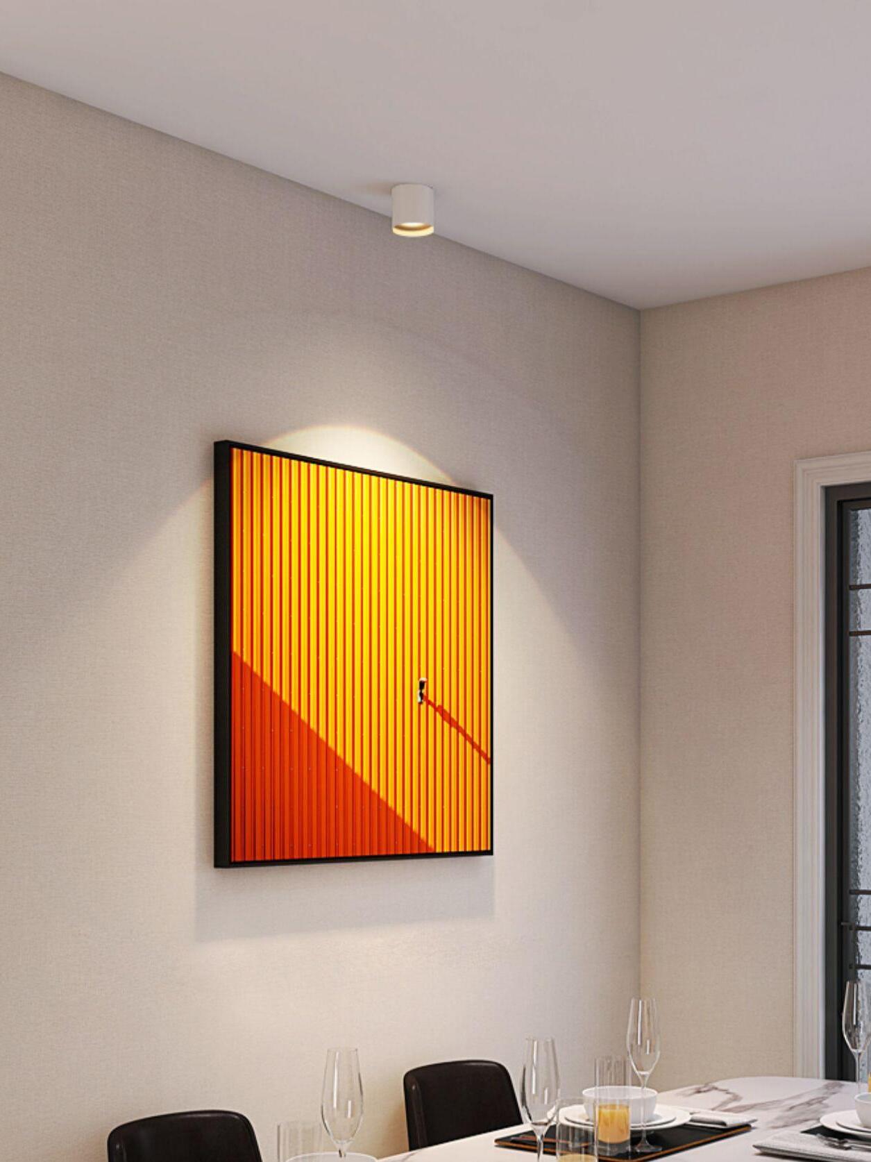 White ceiling light above an orange architectural print near a dining table with glassware