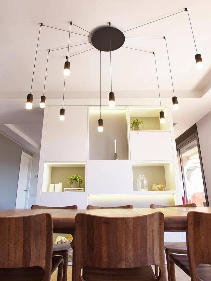 Black radial pendant arrangement above dining chairs and illuminated wall display shelves