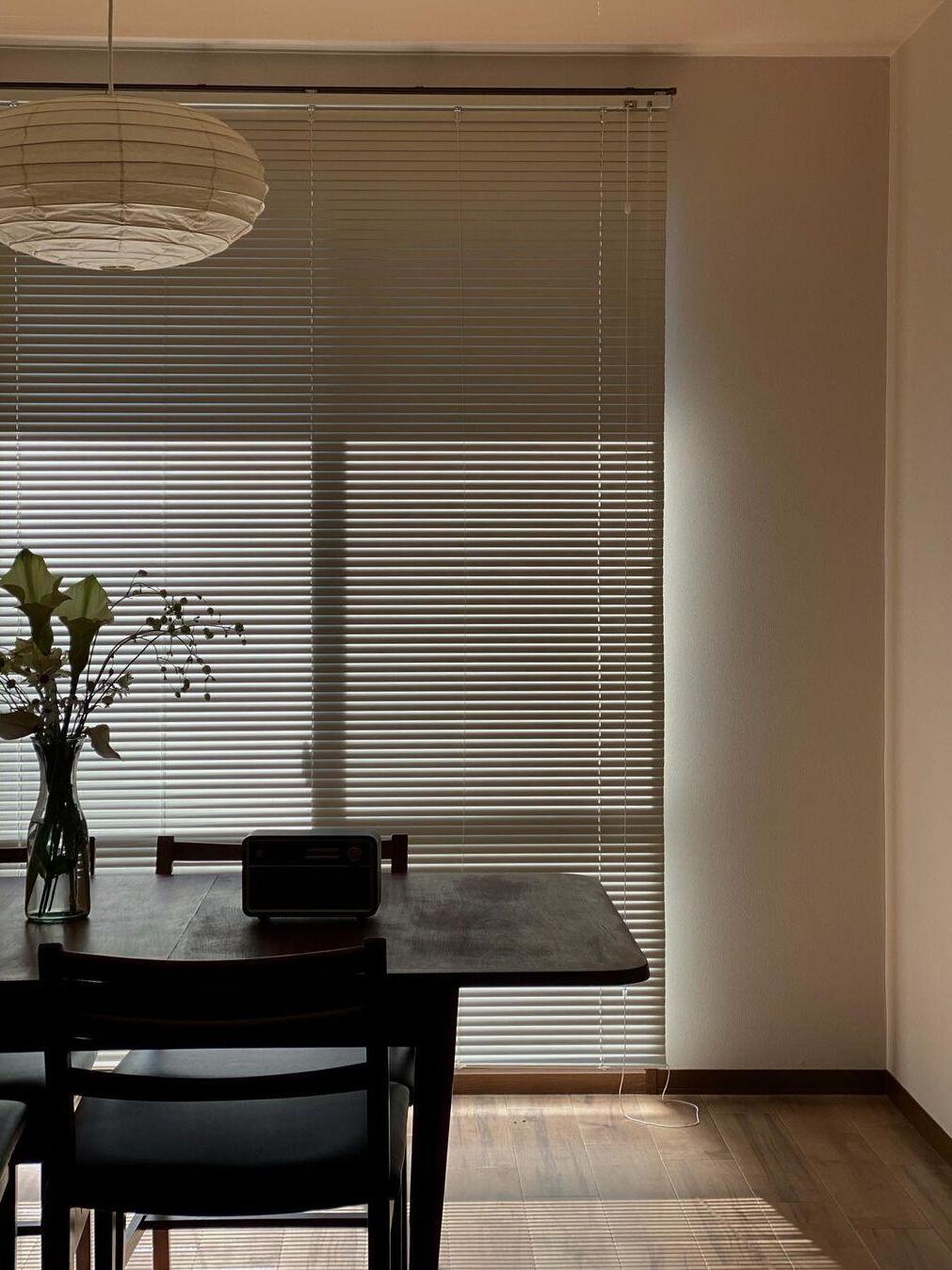 Partly cropped paper lantern over a dark dining table, flower vase and small radio in front of horizontal blinds