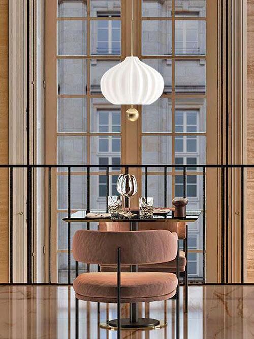 Single white fluted pendant with brass ball above a restaurant table, wine glasses and a pink chair by a window