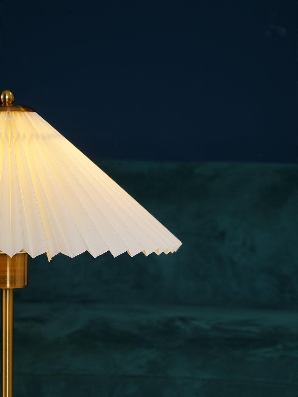 Detail of the lit shade edge and cylindrical gold-tone fitting against a green sofa