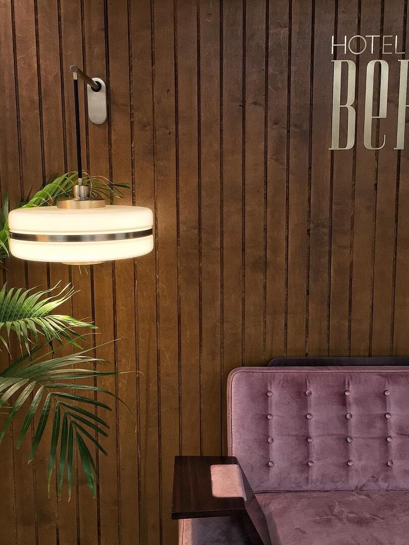 Lit hanging drum wall shade beside plant and pink seat against wood wall
