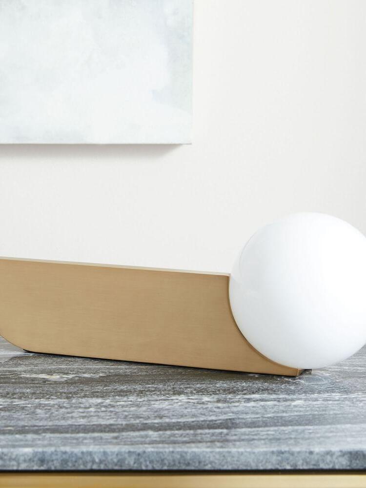 Unlit white globe and gold-colour blade lying horizontally on a dark marble-looking surface