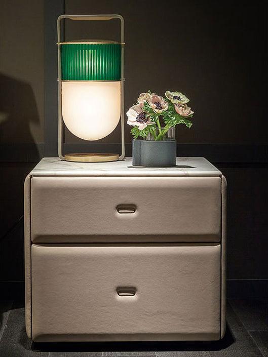 Green ribbed-glass Xi lamp illuminated on a two-drawer bedside cabinet next to a vase of flowers