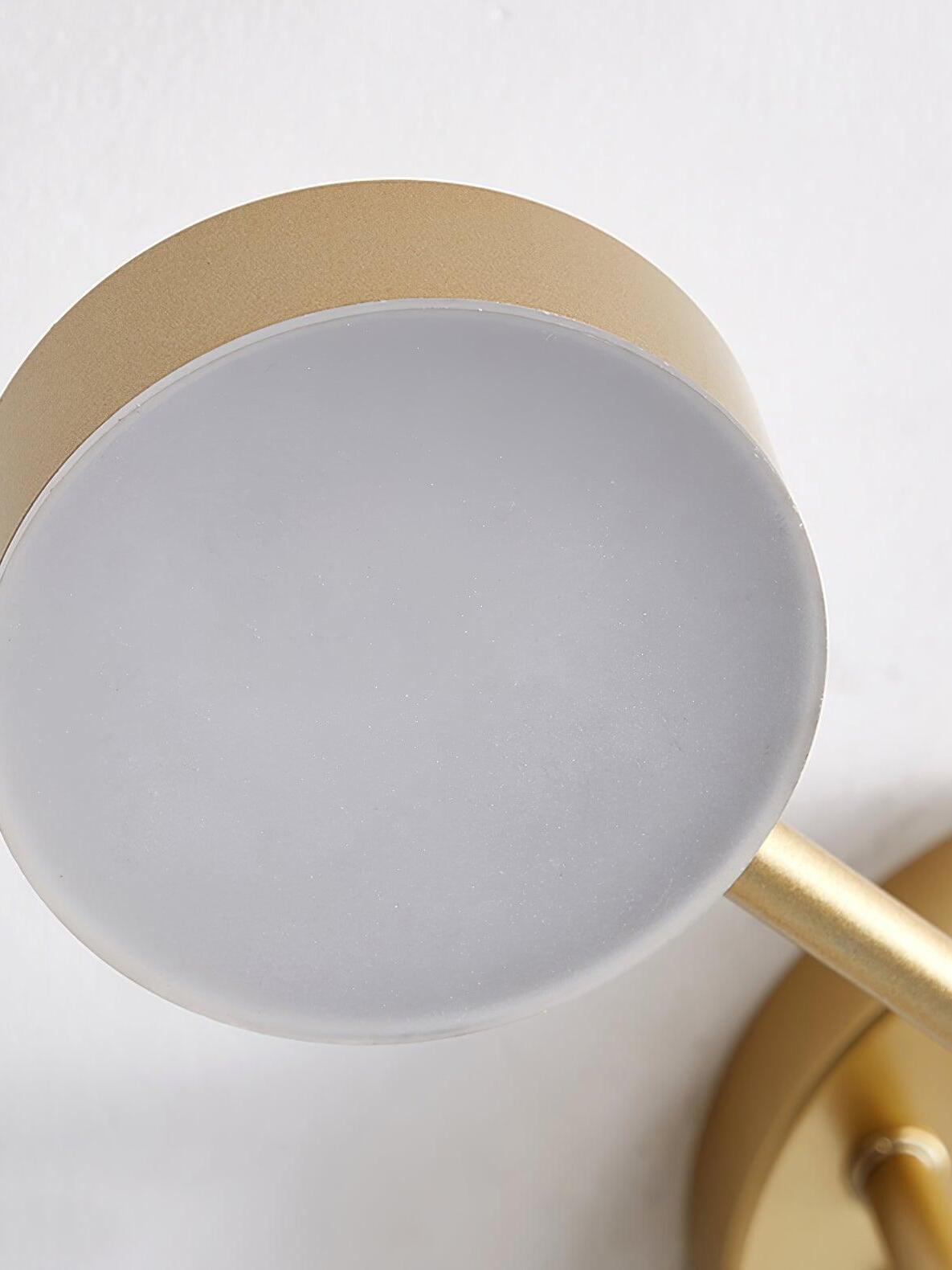 Close-up of an unlit pale circular diffuser in a shallow gold housing, with arm and canopy partly visible