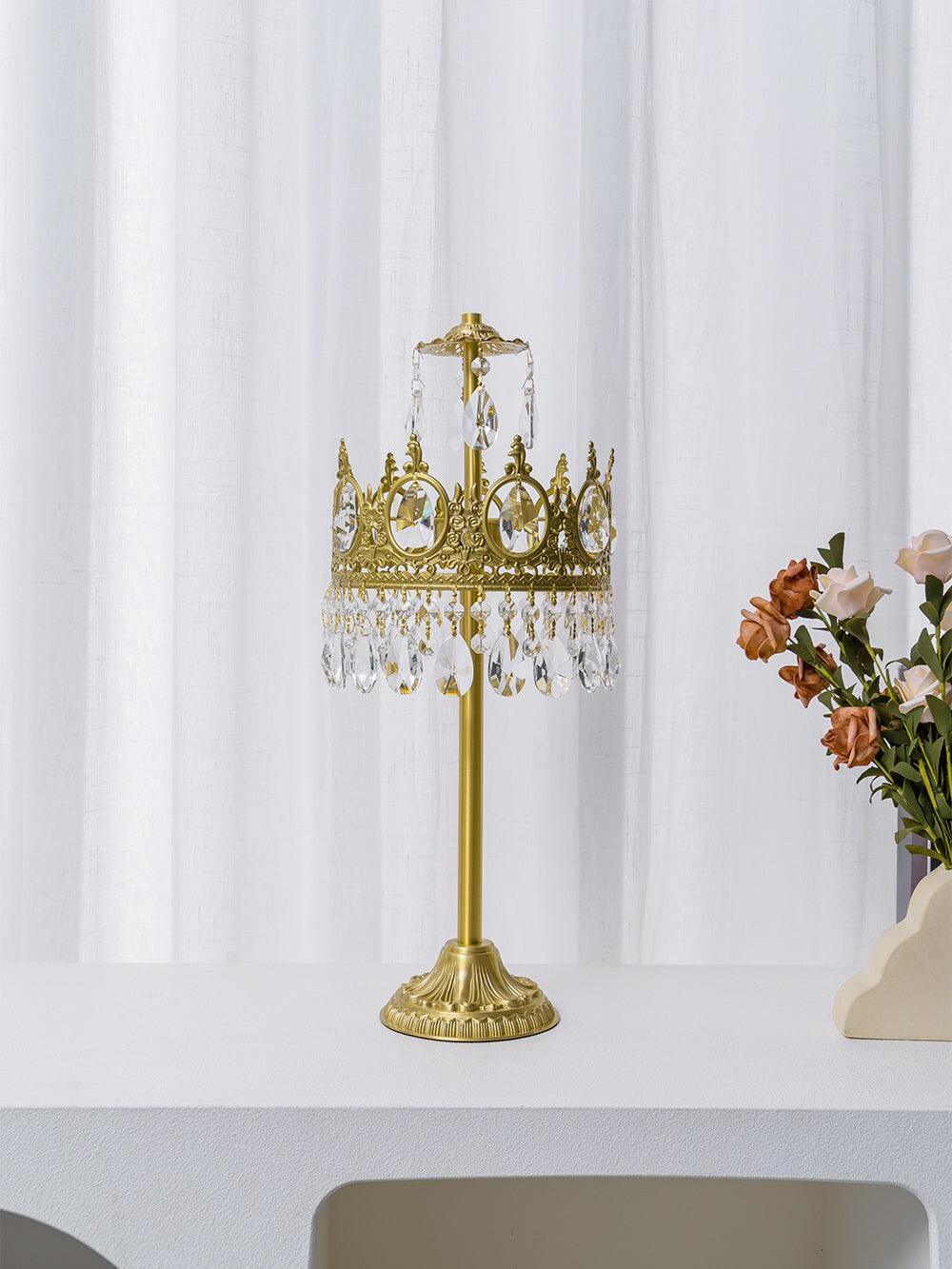 Unlit crystal table lamp on a white console beside flowers and sheer curtains.