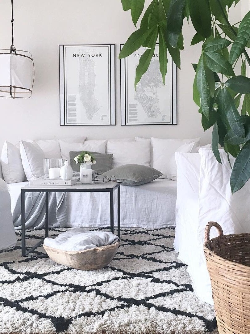 Cropped white lantern pendant above white sofa and black-framed coffee table, with framed maps and leafy plant