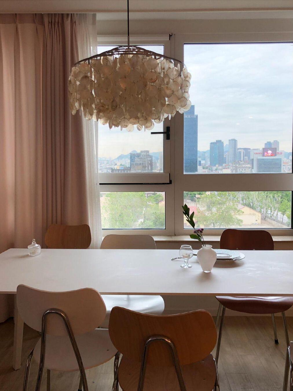 Shell-disc fixture above a table by a city-view window