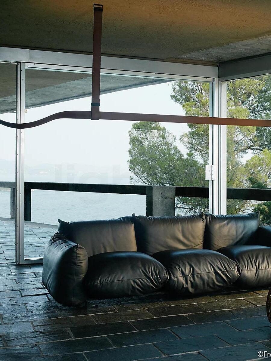 Brown horizontal pendant with a curved strap end above a black leather sofa beside a window overlooking water