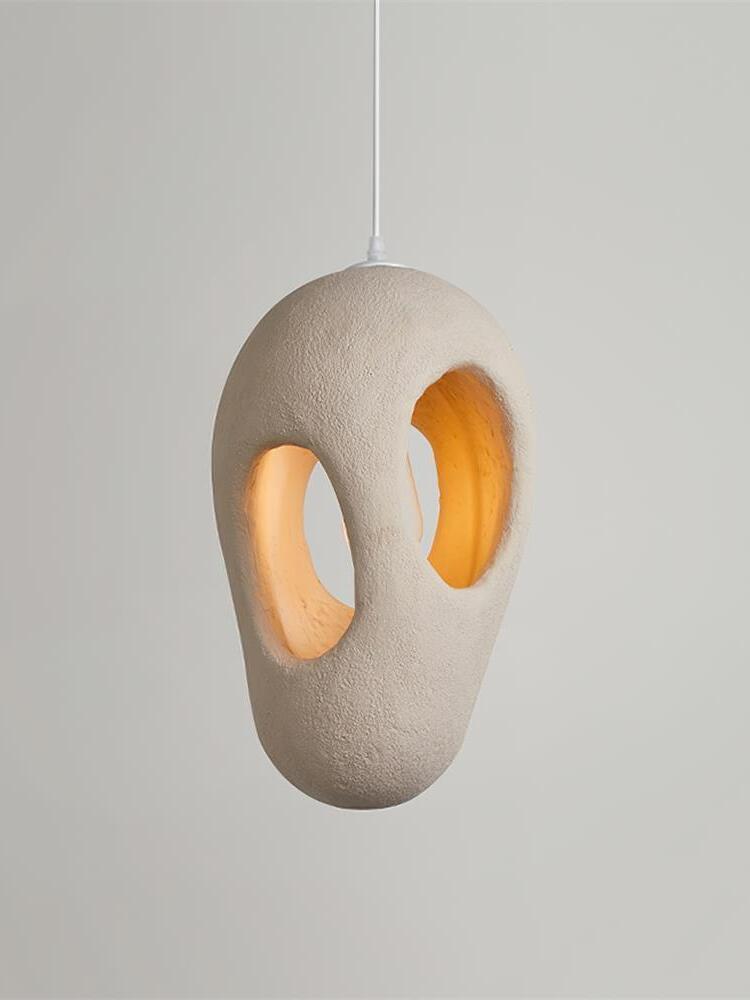 Elongated cream-looking textured pendant with two large openings glowing warm inside on a White cord against Gray