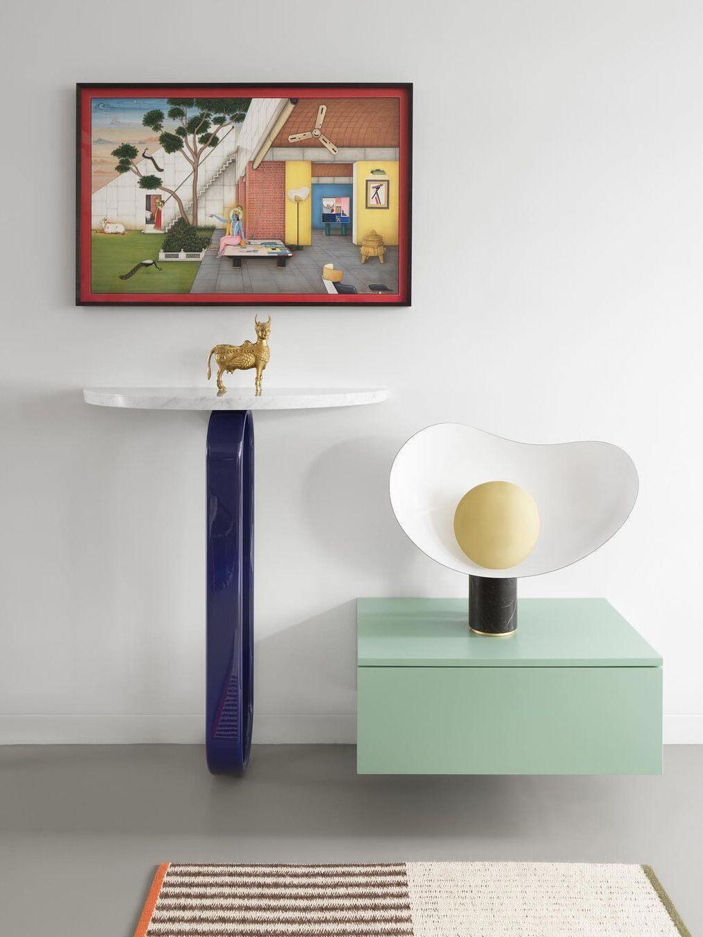 Table lamp on low green cabinet beneath framed art