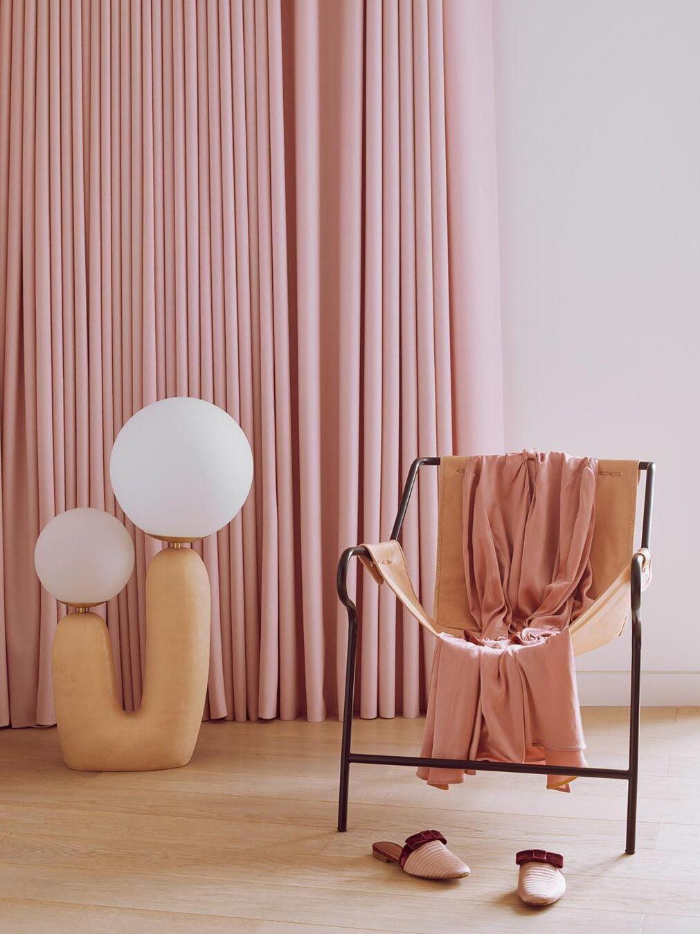 Tall pale U-shaped lamp beside pink curtains