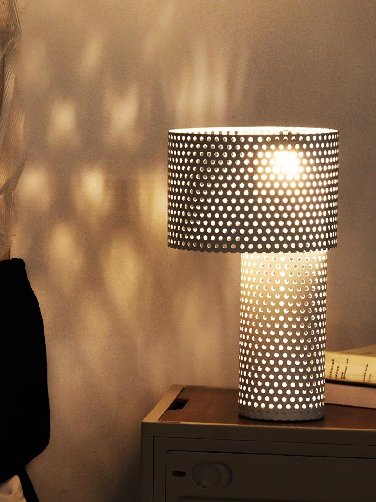 Lit perforated table lamp casting dots above bedside cabinet