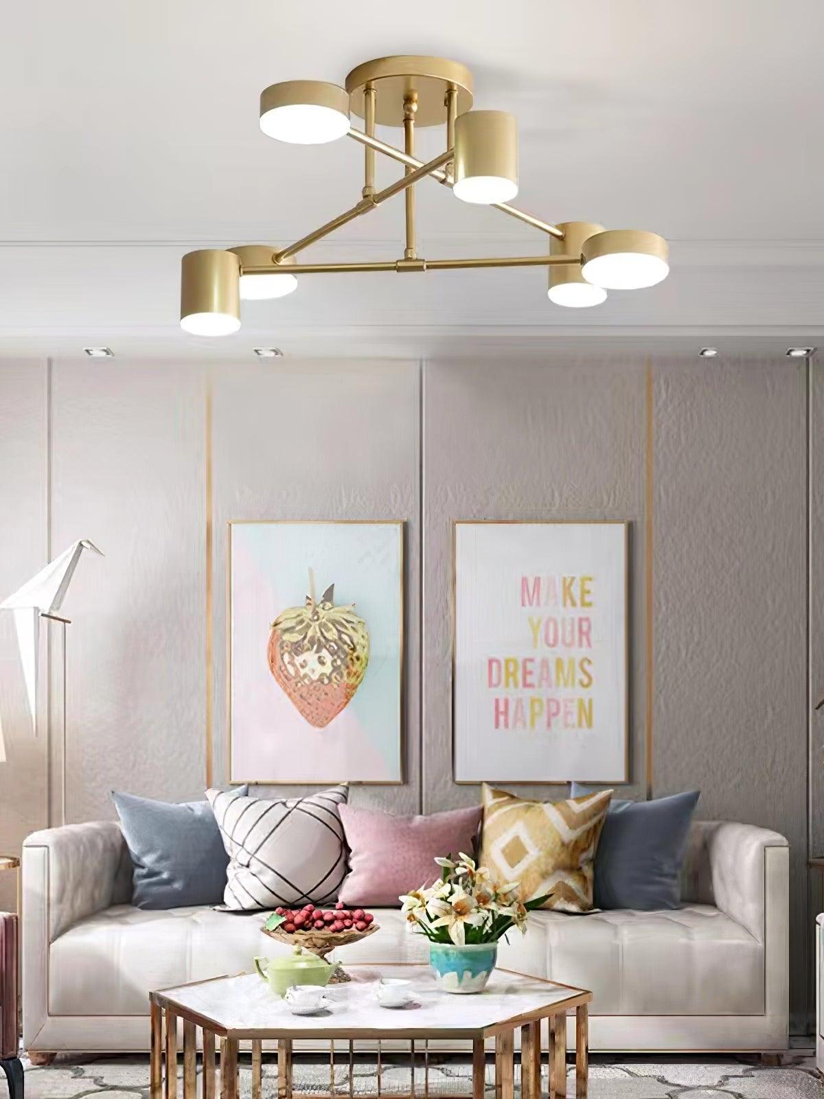 Gold six-head ceiling light above a white sofa, colorful cushions, flowers and a gold-edged coffee table