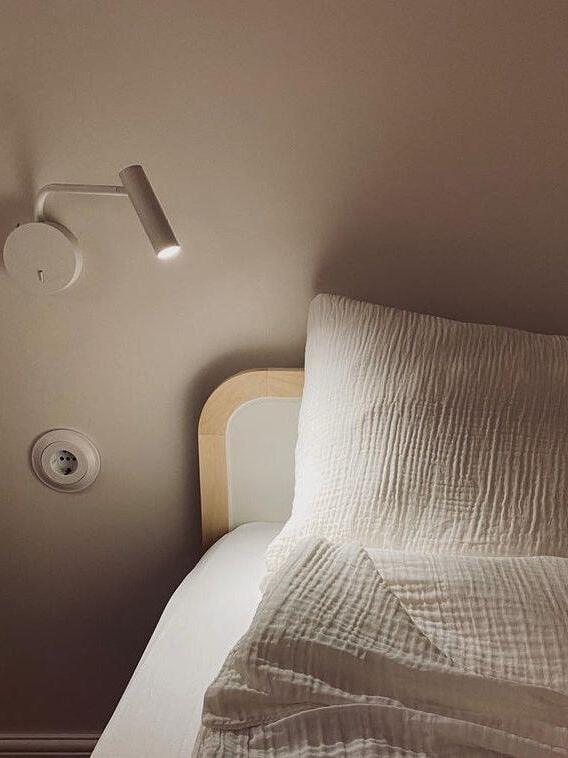 White reading sconce beside pillows and a headboard