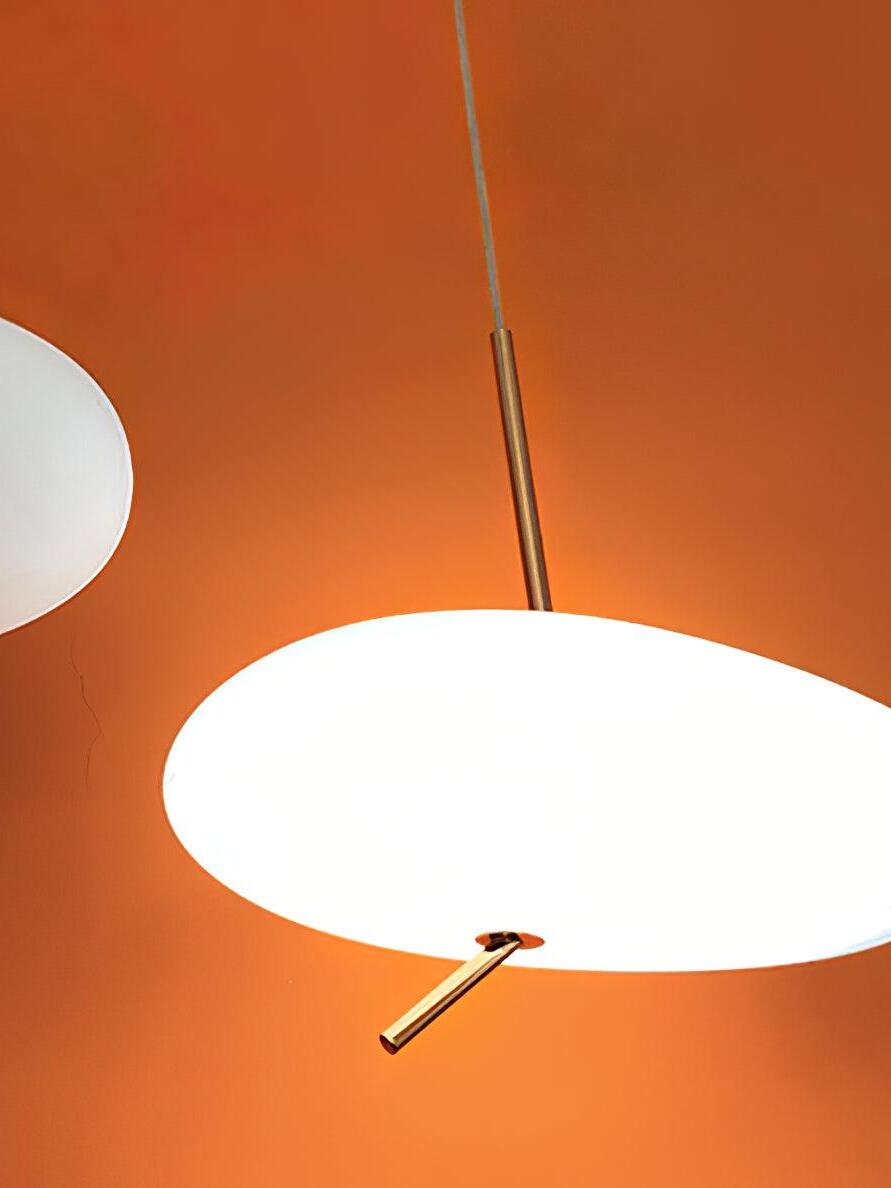 Close view of a lit white shade and angled rose-gold lower stem against an orange background