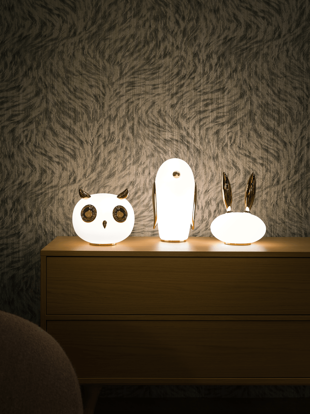 Owl, penguin and rabbit lamps spaced across wood sideboard