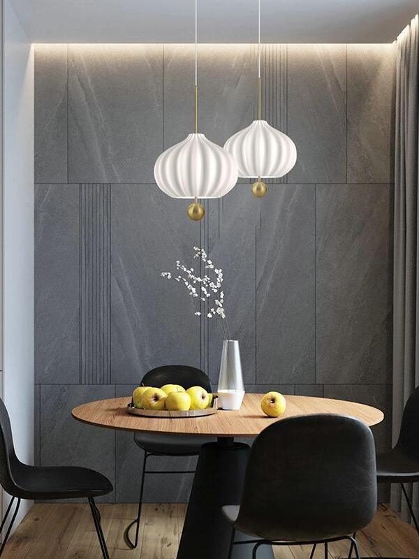 Two white fluted glass pendants at staggered heights above a round wooden table with fruit and a blossom vase