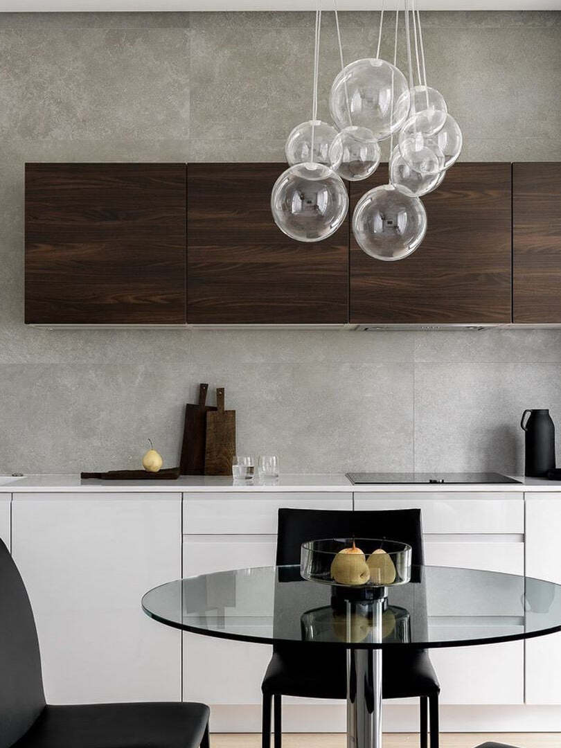 Clear glass globe arrangement above a round glass table with a fruit bowl, black chairs and white kitchen cabinets