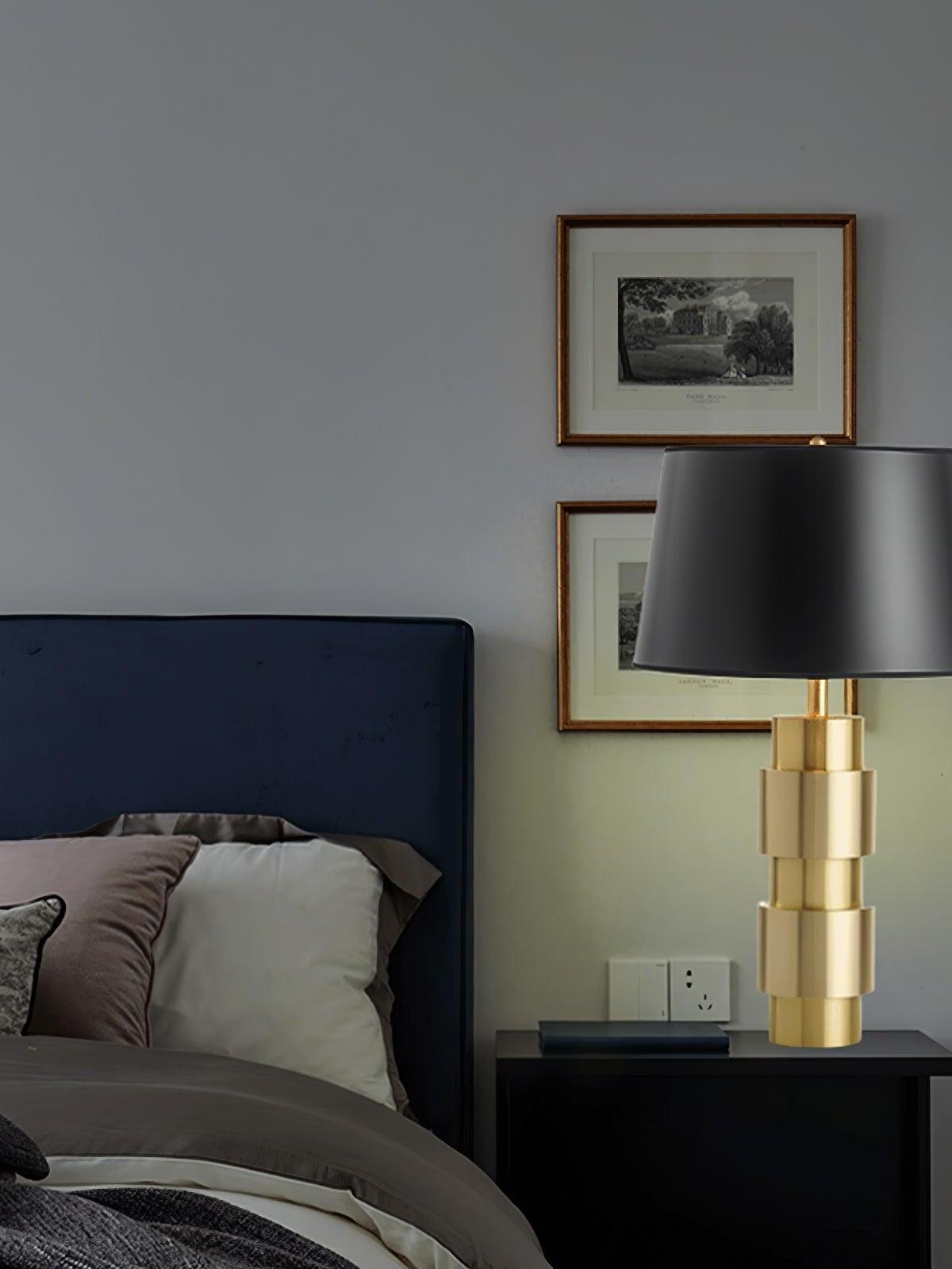Gold-tone Jean lamp on a dark cabinet beside a bed and framed landscape pictures